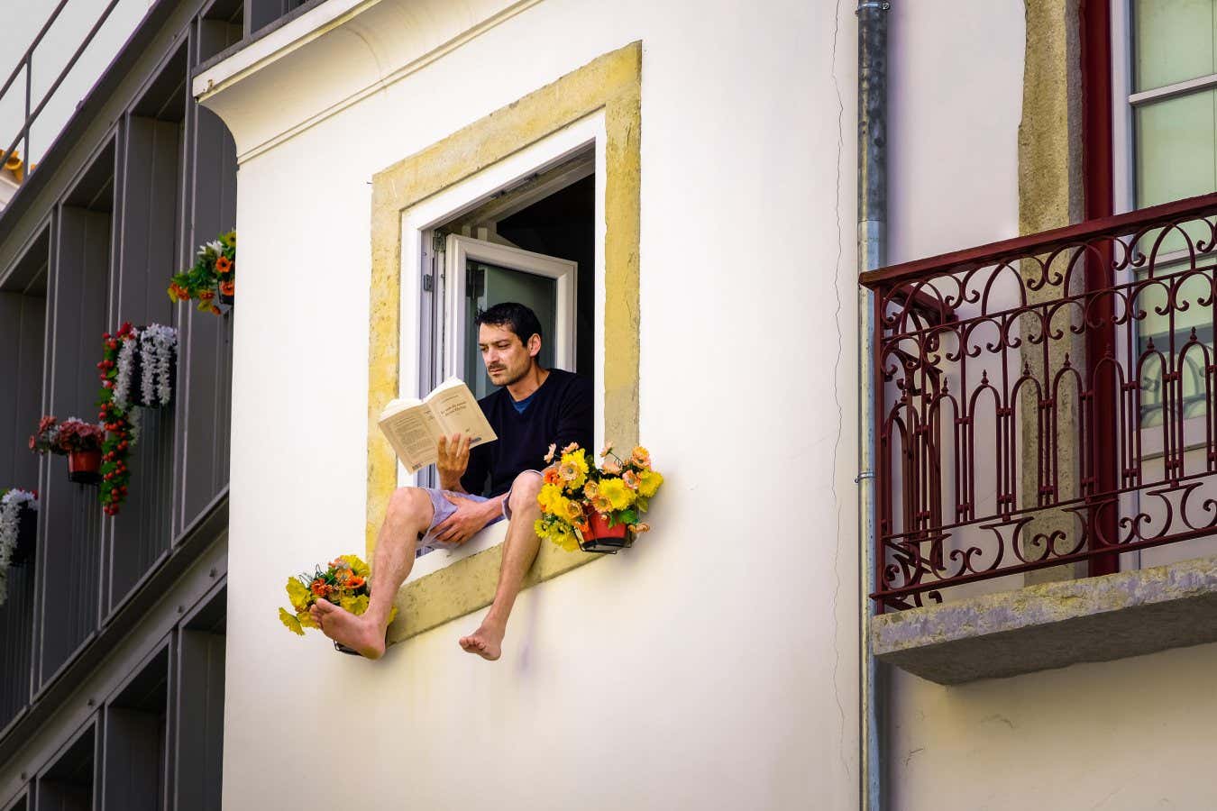 MP46X7 Man sitting on the window seal of an open window reading; man's legs dangling out of window